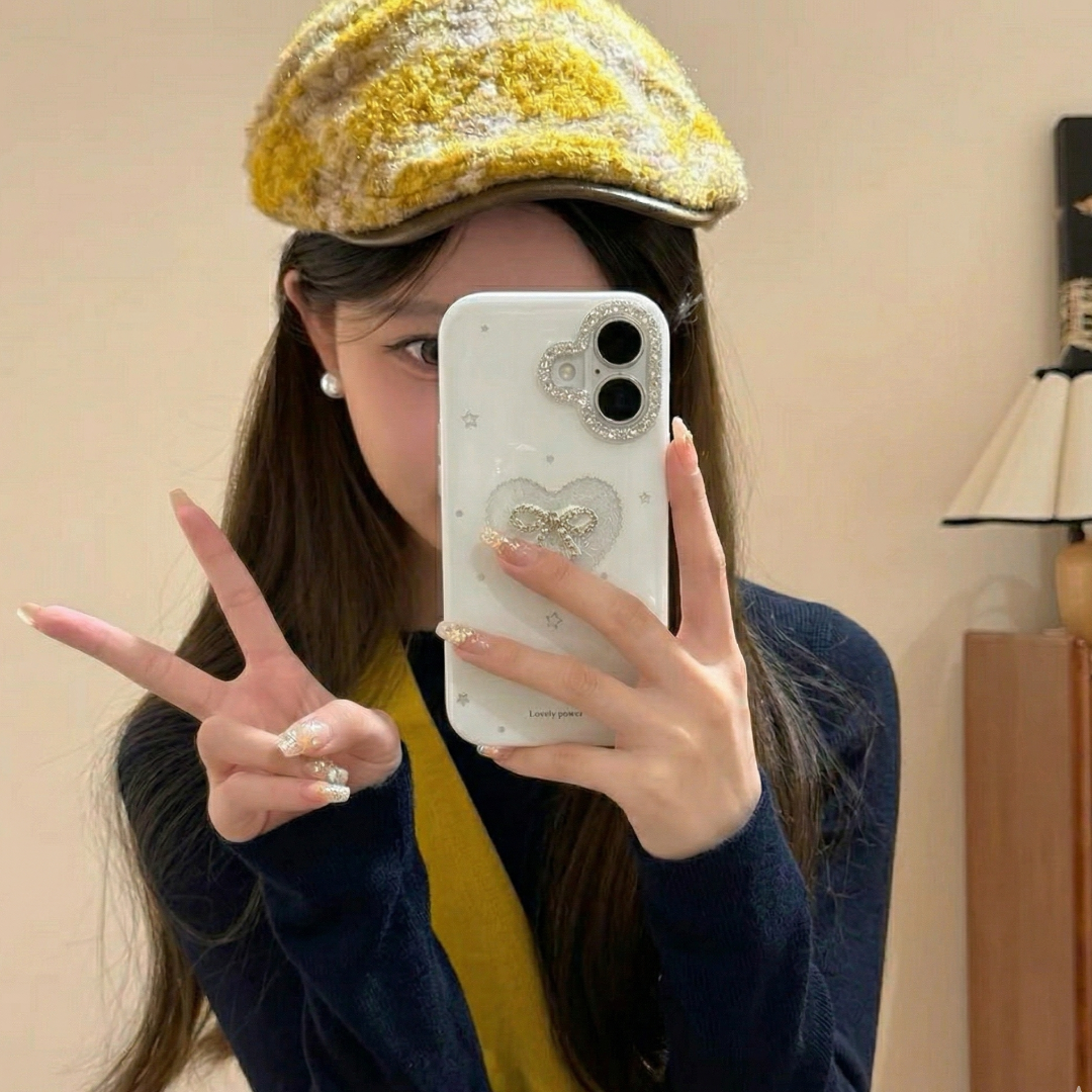 Person wearing a yellow checkered hat and blue jacket, holding a phone with a heart case.